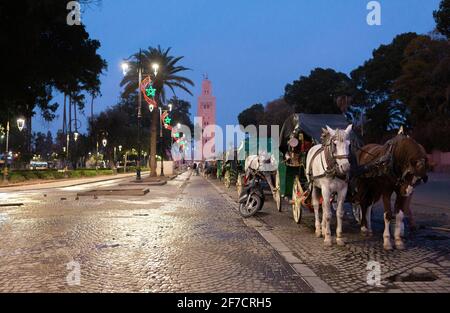 Buggy trainato da cavalli e la moschea di Koutoubia sullo sfondo la mattina presto a Marrakech, Marocco Foto Stock