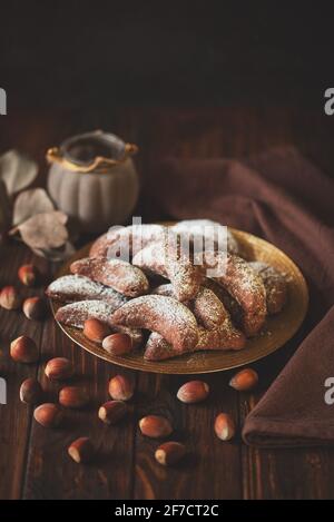 Biscotti fatti in casa nocciole crescent di cioccolato con zucchero in polvere su sfondo di legno marrone. Spazio di copia. Messa a fuoco morbida Foto Stock