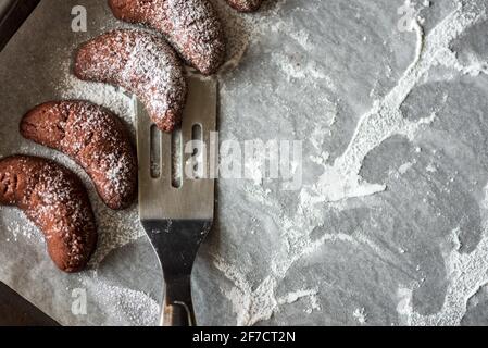 Teglia da forno con biscotti fatti in casa con nocciole a mezzaluna di cioccolato e polvere di zucchero su fondo di legno marrone. Vista dall'alto. Messa a fuoco morbida Foto Stock