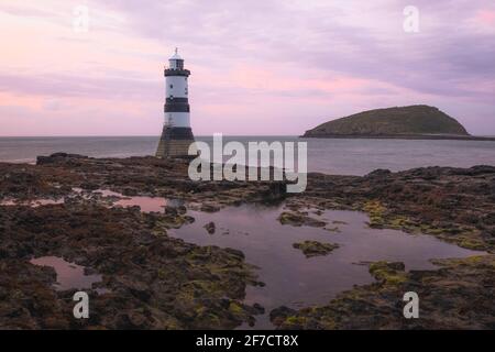 Colorato idilliaco cielo rosa tramonto o alba mare a Penmon Point e Trywn Du Lighthouse lungo la costa rocciosa di Anglesey, Galles del Nord, Regno Unito. Foto Stock