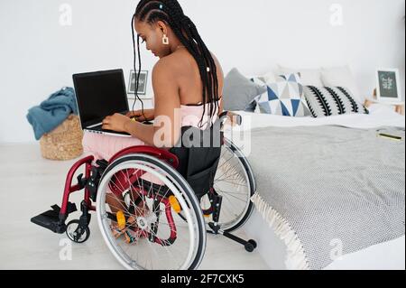 Giovane donna afroamericana disabile in sedia a rotelle a casa che lavora con un computer portatile. Foto Stock