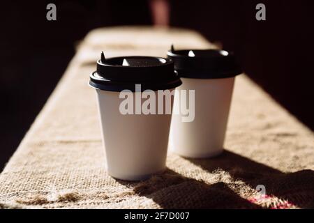 Due tazze di carta da caffè libbra sul burlap. Tazza da asporto di caffè in chicchi Foto Stock