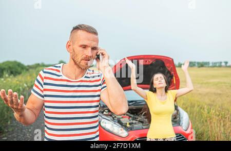 Una macchina rotta. Una giovane coppia sta cercando di chiedere aiuto in caso di guasto di un'auto. Foto Stock