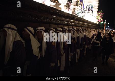 I Cucuruchos in abiti viola si processano solennemente per le strade di Antigua, Guatemala, durante le tradizionali celebrazioni della settimana Santa di Semana. Foto Stock