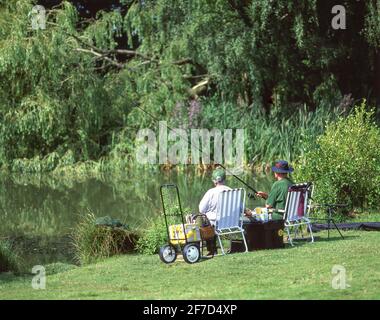 La coppia anziana pesca in piccolo lago d'acqua dolce, Stanwell Moor, Surrey, Inghilterra, Regno Unito Foto Stock