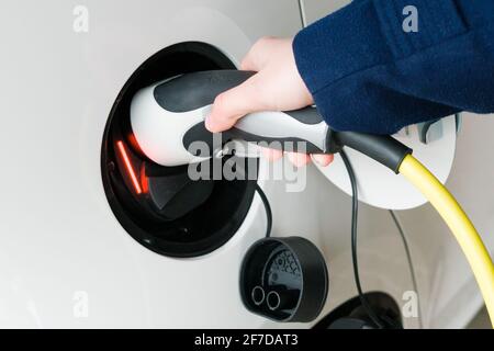 Donna inserisce il cavo di alimentazione in un'auto elettrica per la ricarica Foto Stock