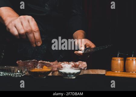 Marinare gli spiedini del collo di maiale, aggiungere sale, curry e basilico alla carne, pezzi di carne su una tavola di legno.2020 Foto Stock