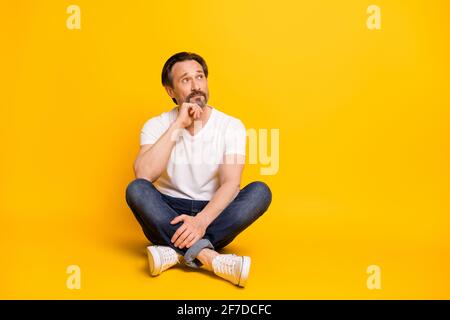 Foto a corpo pieno di un uomo affascinante, che guarda spazio vuoto dream tenere mento a mano isolato su sfondo giallo Foto Stock