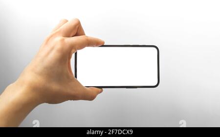 Mano che tiene in orizzontale lo smartphone con schermo bianco vuoto, foto di concetto mockup del telefono cellulare Foto Stock