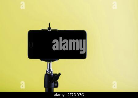 Smartphone collegato a un treppiede su sfondo giallo. Concetto di selfie e blogging Foto Stock