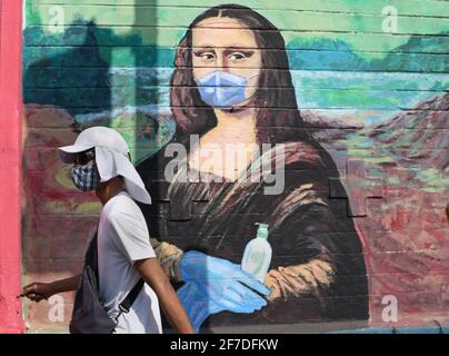 Un uomo che indossa un cappuccio e una maschera protettiva passa accanto a un graffiti dipinto per creare consapevolezza sulla malattia di coronavirus a Mumbai.a causa dell'aumento dei casi di coronavirus nello stato di Maharashtra, il governo ha imposto il coprifuoco notturno dalle 20:00 alle 7:00 per frenare la diffusione del coronavirus. Foto Stock