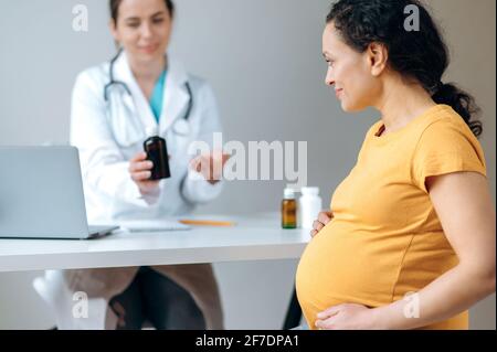 Il medico consiglia e prescrive farmaci per la donna incinta. Razza mista, donna incinta matura, seduta su appuntamento del medico, in fase di prevenzione medica e trattamento.concetto sanitario Foto Stock