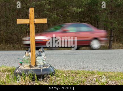Una croce commemorativa a bordo strada con candele che commemorano la tragica morte, su un giro di fondo auto offuscata. Foto Stock