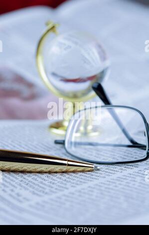 Occhiali, penna, globo giacciono su un giornale Foto Stock