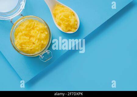 Scrub del corpo giallo fatto in casa in un vaso di vetro su sfondo blu. Vista dall'alto, spazio di copia per il testo. Concetto DI SPA. Messa a fuoco selettiva Foto Stock