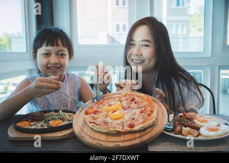 Madre e figlia sorridenti felici con colazione e pizza in ora del mattino Foto Stock