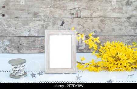 Sagoma vuota del telaio in legno. Mazzo di fiori di forsizia gialli, nastro a stella su tavolo con tovaglia bianca. Sfondo di legno. Concetto di primavera Foto Stock