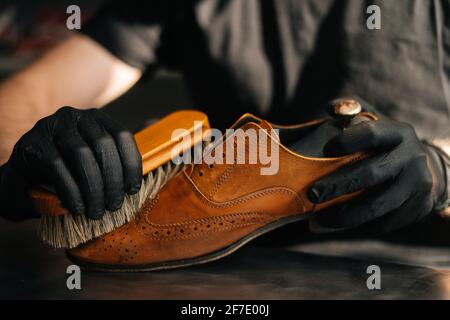 Mani ravvicinato di pulizia da calzolaio irriconoscibile con la spazzola vecchie scarpe in pelle marrone chiaro. Foto Stock