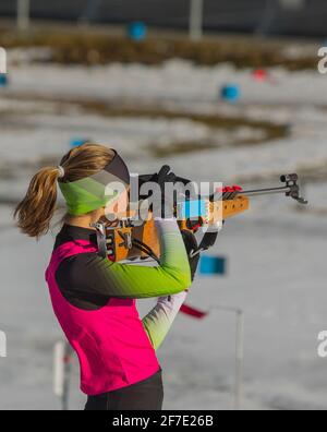 La corsa femminile del biathlon sta in piedi sulla terra e sta puntando il suo fucile. Donna biatleta su un poligono di tiro, sparando in piedi. Foto Stock