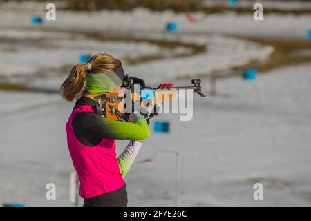 La corsa femminile del biathlon sta in piedi sulla terra e sta puntando il suo fucile. Donna biatleta su un poligono di tiro, sparando in piedi. Foto Stock