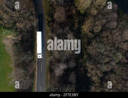 Lungo camion bianco sta viaggiando attraverso la foresta in autunno su una strada stretta. Drone immagine aerea di un camion da sopra.ž Foto Stock