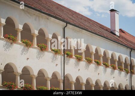 Passerella ad arco con fiori sul balcone, facciata anteriore bianca visibile di un vecchio edificio o castello con una fila di archi al primo e secondo piano e. Foto Stock