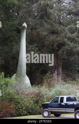 Una statua brontosauro sembra emergere dalla foresta accanto a un camion presso i giardini preistorici di Port Orford, Oregon. Foto Stock