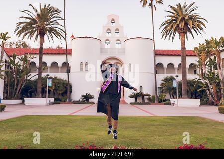 Uomo che salta, indossando un abito/cappuccio di graduazione. Foto Stock