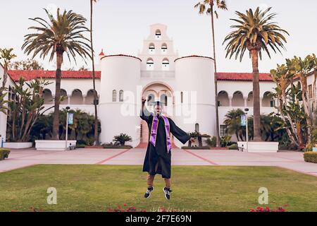 Uomo che salta, indossando un abito/berretto di laurea all'università. Foto Stock