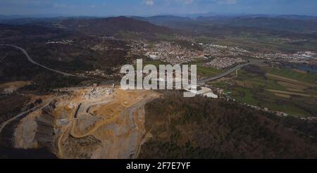 Panorama di un drone aereo di una miniera o cava aperta in una giornata di sole a Verd, Slovenia. Terrazze visibili e vasta superficie di sabbia e pietre, con una città dentro Foto Stock