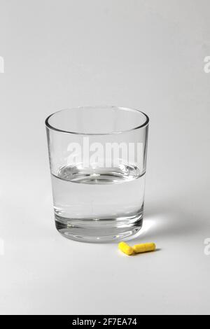 Immagine di un bicchiere d'acqua e di due compresse pronte per essere prese su uno sfondo bianco con spazio per la copia. Medicina e farmaci. Foto Stock