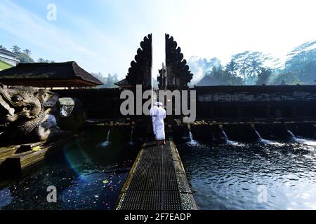 Sacerdote indù balinese che prega presso la piscina purificante del tempio Tirta Empowerl di Bali, Indonesia. Foto Stock