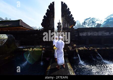 Sacerdote indù balinese che prega presso la piscina purificante del tempio Tirta Empowerl di Bali, Indonesia. Foto Stock
