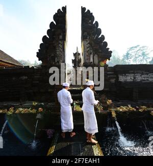Sacerdote indù balinese che prega presso la piscina purificante del tempio Tirta Empowerl di Bali, Indonesia. Foto Stock