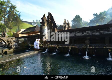 Sacerdote indù balinese che prega presso la piscina purificante del tempio Tirta Empowerl di Bali, Indonesia. Foto Stock