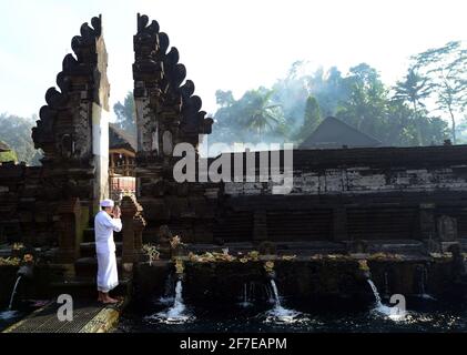 Sacerdote indù balinese che prega presso la piscina purificante del tempio Tirta Empowerl di Bali, Indonesia. Foto Stock
