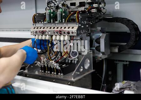 Il tecnico di sesso maschile esegue lavori di manutenzione su una stampante di grande formato in tessuto da pavimento. Foto Stock