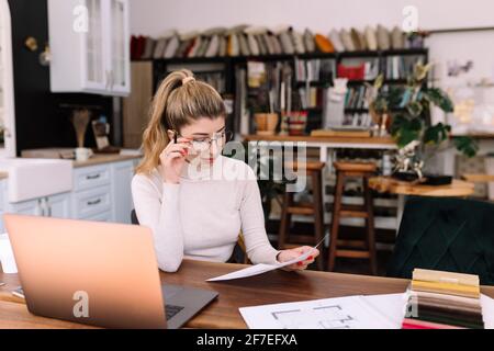 Un interior designer sta lavorando a un nuovo progetto. Creazione di uno schizzo. Scelta del colore dalla tavolozza dei colori dei tessuti. Computer portatile su tavolo in legno di quercia Foto Stock