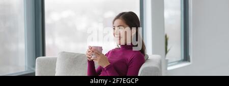 Felice donna asiatica rilassante bere caffè tazza seduta in confortevole soggiorno. Banner panoramico stile di vita domestico di lusso. Foto Stock