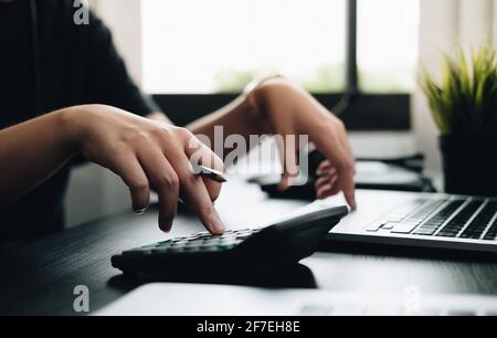 Primo piano mani uomo d'affari facendo le finanze con l'uso della calcolatrice e. computer portatile in ufficio Foto Stock