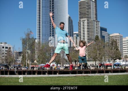 Divertente padre e figlio che saltano in città sullo sfondo. Concetto di bambino di infanzia e di paternità. Felice padre e figlio che giocano insieme all'aperto. Famiglie urbane. Foto Stock