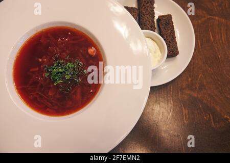 Un piatto tradizionale di cucina Russa e Ucraina. Borscht con erbe, panna acida e crostini all'aglio. Su un tavolo di legno con spazio per la copia Foto Stock