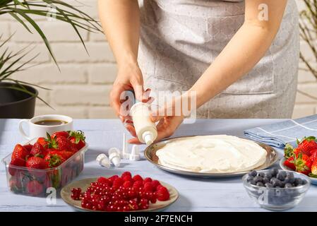 la panettiera donna strizza la panna montata. Torta di fragole fatta in casa con torta di meringa e crema con fragole. Foto Stock