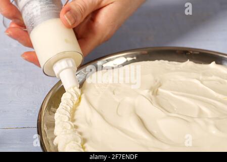 la panettiera donna strizza la panna montata. Torta di fragole fatta in casa con torta di meringa e crema con fragole. Foto Stock