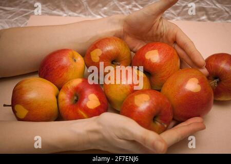 Persona che tiene in mano gustose e deliziose mele rosse e verdi. Le mele hanno un cuore su di loro, buono come una valentine presente o concetto di cibo sano. Foto Stock