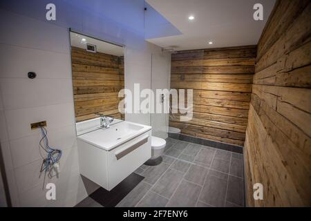 Un bagno moderno con pareti in legno e piastrelle grigie sul pavimento. Piastrelle bianche sul pavimento, un po' di specchio e una cabina doccia con parete di vetro. Look elegante Foto Stock