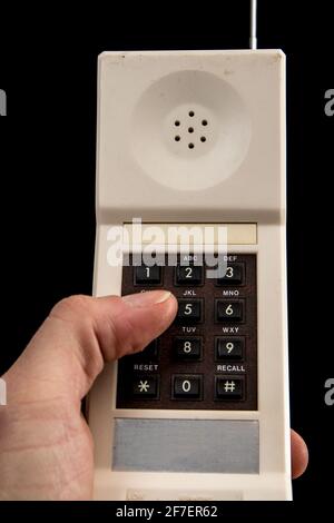 Un vecchio telefono cordless bianco d'epoca degli anni '80 isolato in nero con un dito che compone un numero. Pollice visibile, tastiera marrone e argento A. Foto Stock