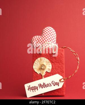 Piccola borsa di carta con una forma a cuore a scacchi su sfondo rosso, concetto di giorno Happy Mothers Foto Stock