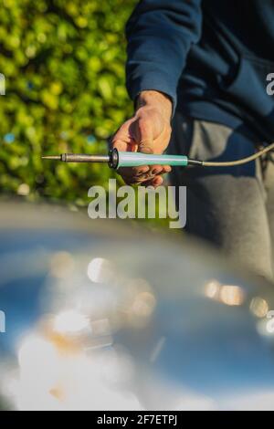 Man saldando i fili nel vano motore di un'auto. Auto moderna con riparazioni eseguite da un meccanico domestico. Caucasica che tiene una saldatrice professionale del filo. Foto Stock