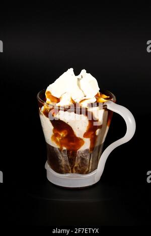 Cioccolata calda o bevanda al caffè in una tazza di vetro con supporto, isolato di nero. Briciole di cocco visibili, latte, panna montata e altri ingredienti dolci. Foto Stock